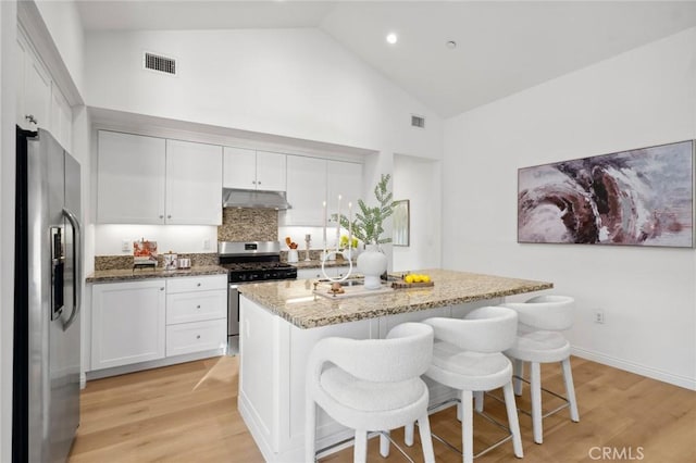 kitchen featuring stainless steel appliances, under cabinet range hood, high vaulted ceiling, light wood-style flooring, and light stone countertops