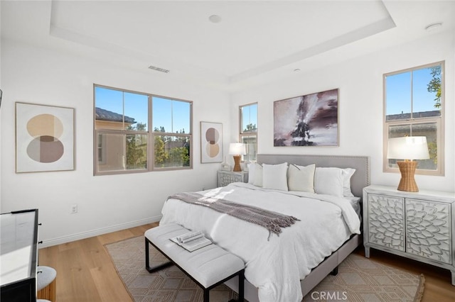 bedroom with a tray ceiling, multiple windows, and wood finished floors