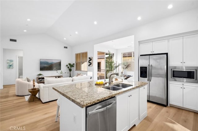 kitchen featuring stainless steel appliances, a sink, a kitchen island with sink, light wood-style floors, and light stone countertops