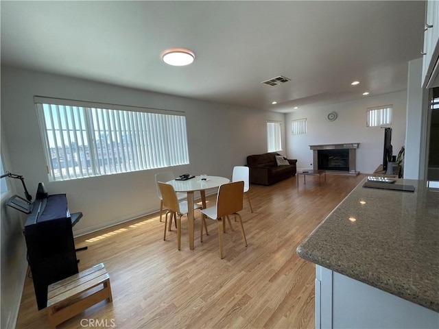 dining room with a fireplace, healthy amount of natural light, light wood-style flooring, recessed lighting, and baseboards