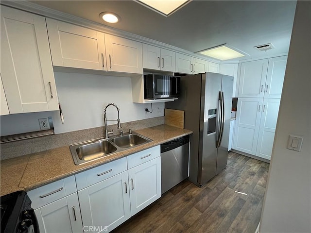 kitchen featuring appliances with stainless steel finishes, a sink, white cabinets, dark wood-type flooring, and recessed lighting