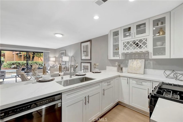 kitchen featuring dishwasher, a sink, gas stove, open floor plan, and white cabinetry