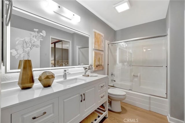 bathroom featuring vanity, wood finished floors, toilet, and bath / shower combo with glass door