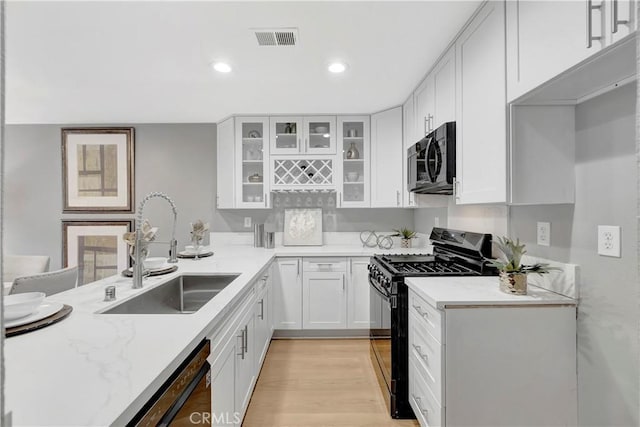 kitchen with black appliances, a sink, light stone counters, glass insert cabinets, and recessed lighting