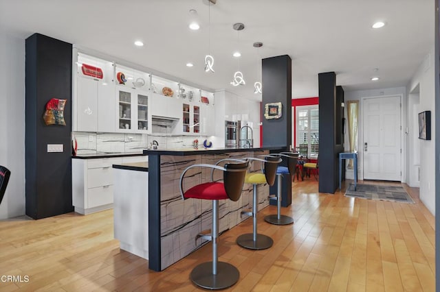 1524 Seabridge Ln, Oxnard, CA 93035 - kitchen with dark countertops, light wood-style flooring, white cabinets, backsplash, and pendant lighting