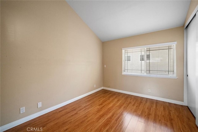 unfurnished room with wood finished floors, baseboards, and lofted ceiling