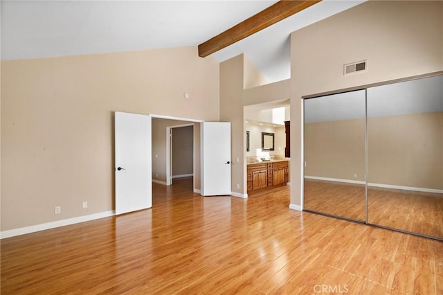 unfurnished bedroom with light wood-style flooring, beam ceiling, high vaulted ceiling, baseboards, and ensuite bath