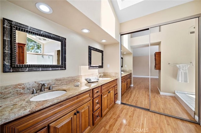 bathroom with wood finished floors, double vanity, a skylight, vaulted ceiling, and baseboards