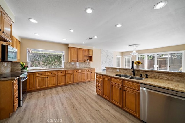 kitchen with appliances with stainless steel finishes, a sink, brown cabinets, light wood-style floors, and recessed lighting