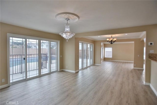 unfurnished living room featuring a chandelier, baseboards, wood finished floors, and crown molding