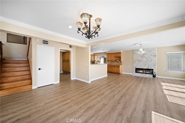 unfurnished living room with a chandelier, stairway, baseboards, recessed lighting, and ornamental molding