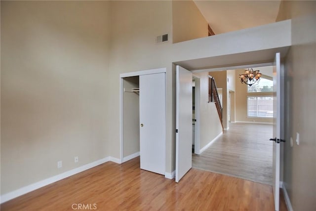 unfurnished bedroom with a chandelier, baseboards, light wood-type flooring, a towering ceiling, and a closet