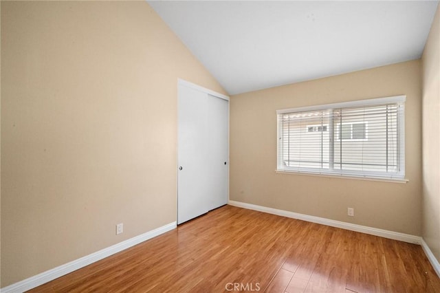 unfurnished room with vaulted ceiling, light wood finished floors, and baseboards