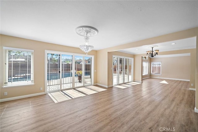 unfurnished living room featuring a chandelier, baseboards, and wood finished floors