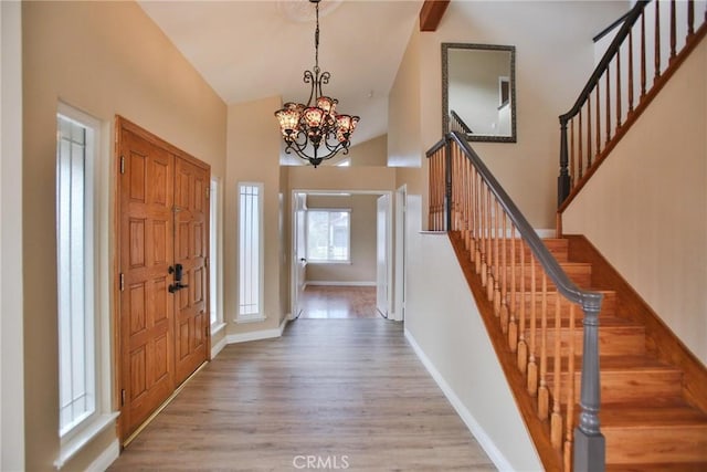 entrance foyer with stairs, light wood-style flooring, a chandelier, baseboards, and high vaulted ceiling