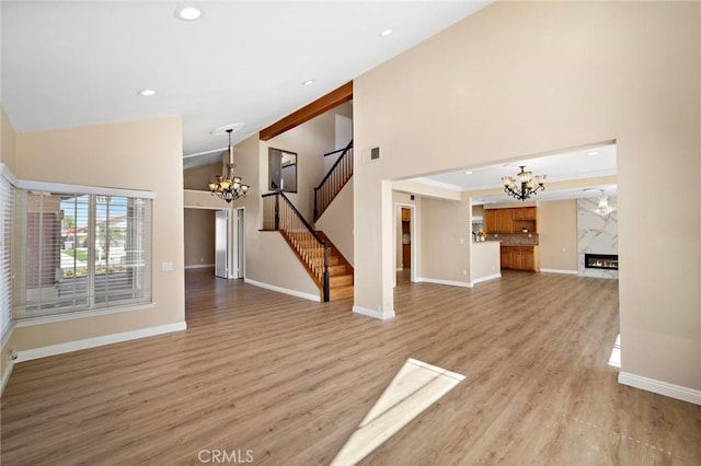 unfurnished living room featuring a chandelier, stairs, high vaulted ceiling, recessed lighting, and baseboards