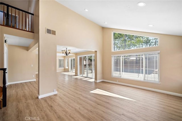 unfurnished living room with baseboards, wood finished floors, a high ceiling, a chandelier, and recessed lighting