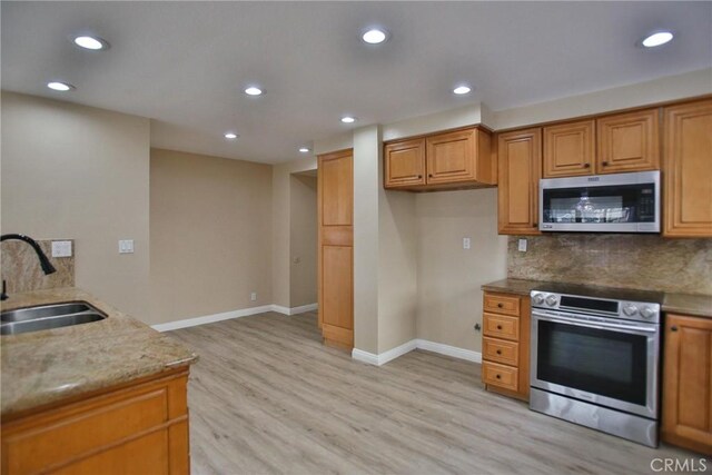 kitchen featuring a sink, stainless steel appliances, light wood-style floors, light stone countertops, and brown cabinets