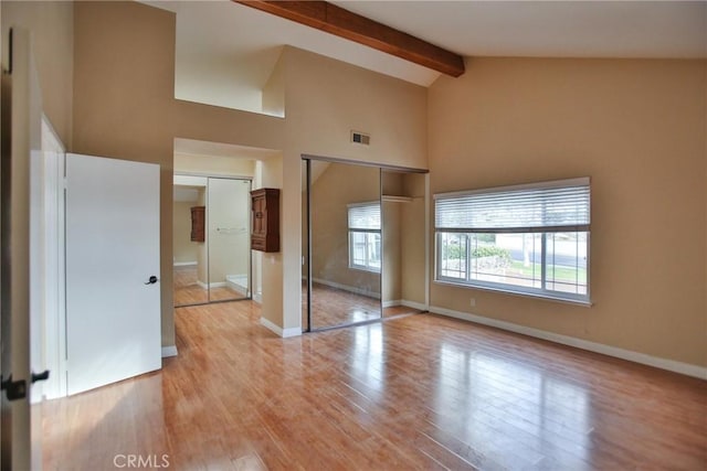 unfurnished bedroom featuring high vaulted ceiling, light wood-type flooring, beam ceiling, and baseboards