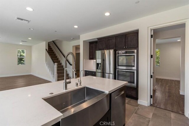 kitchen featuring appliances with stainless steel finishes, a sink, light countertops, dark brown cabinetry, and recessed lighting