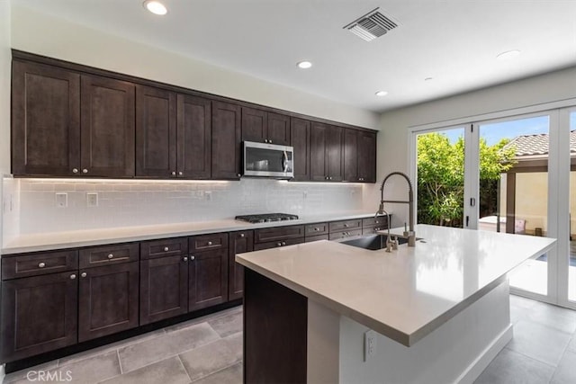 kitchen with stainless steel microwave, a sink, gas cooktop, backsplash, and light countertops