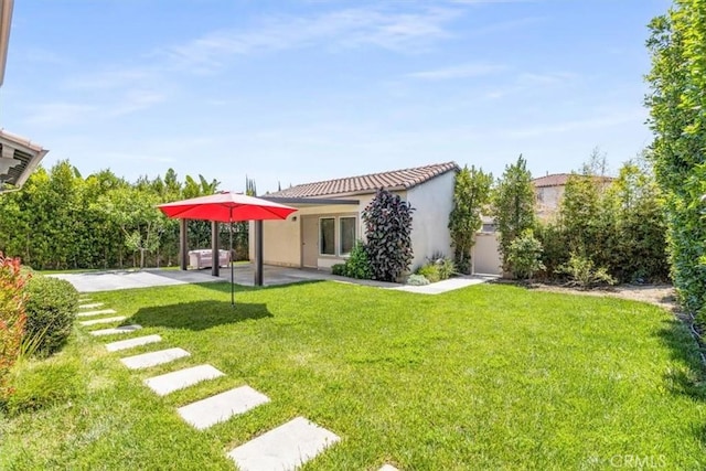 rear view of property with stucco siding, a patio, a yard, and a tiled roof