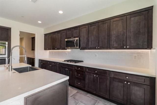 kitchen with appliances with stainless steel finishes, a sink, backsplash, dark brown cabinets, and recessed lighting