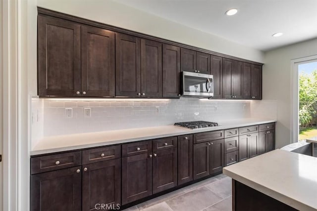 kitchen with stainless steel appliances, dark brown cabinets, backsplash, light countertops, and recessed lighting