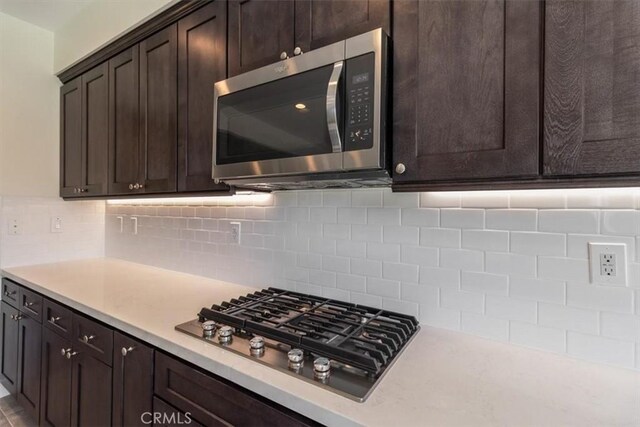 kitchen with appliances with stainless steel finishes, dark brown cabinetry, light countertops, and tasteful backsplash