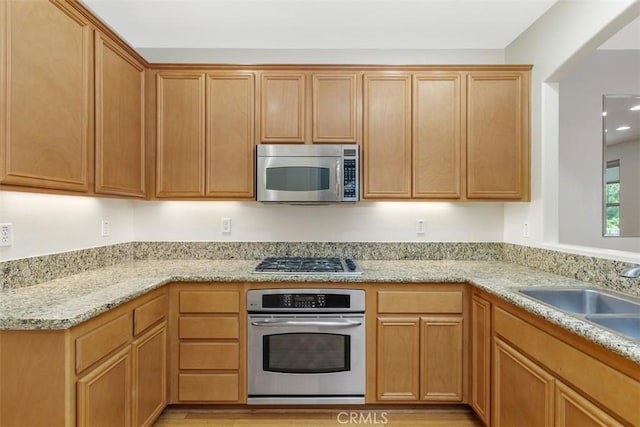 kitchen featuring appliances with stainless steel finishes, a sink, light stone countertops, and light wood finished floors