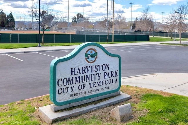 community sign featuring fence and uncovered parking