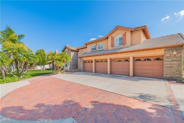 mediterranean / spanish home with decorative driveway, stone siding, an attached garage, a tile roof, and stucco siding
