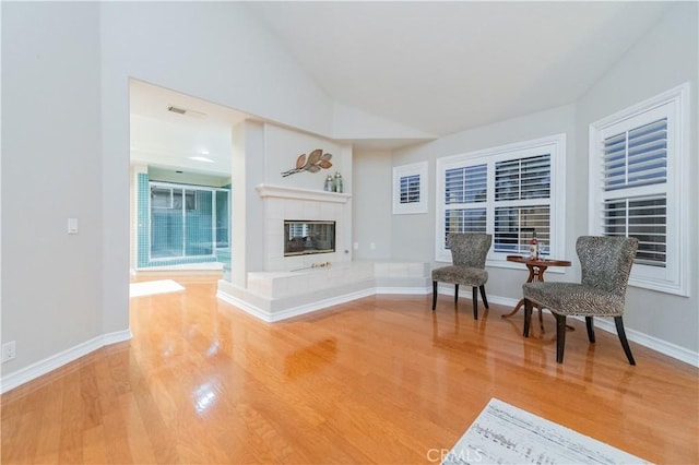 sitting room with light wood-type flooring, a tile fireplace, vaulted ceiling, and baseboards