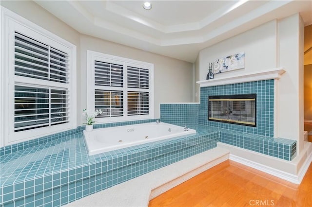 bathroom with a jetted tub, a tray ceiling, a tile fireplace, and recessed lighting