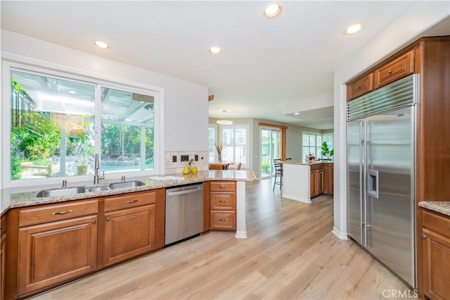 kitchen featuring appliances with stainless steel finishes, a sink, brown cabinetry, light wood-style floors, and recessed lighting