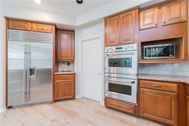 kitchen featuring stainless steel appliances, brown cabinetry, tasteful backsplash, and recessed lighting