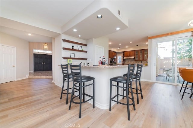 kitchen featuring a breakfast bar area, light wood finished floors, baseboards, recessed lighting, and open shelves