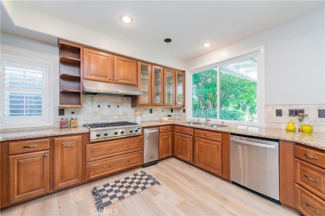kitchen with appliances with stainless steel finishes, under cabinet range hood, a sink, brown cabinets, and recessed lighting