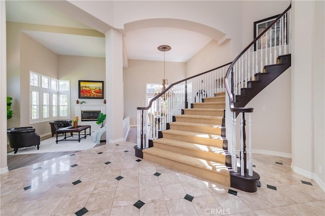 foyer with baseboards, stairs, a glass covered fireplace, a chandelier, and a towering ceiling