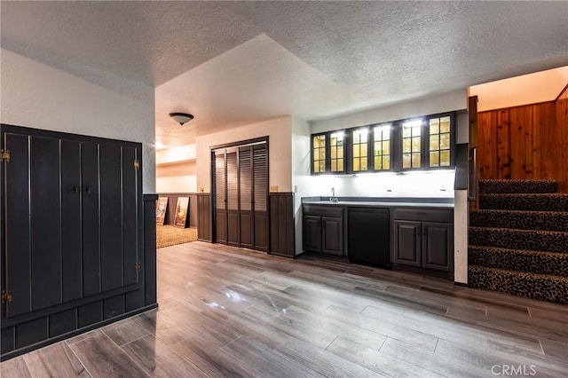 222 Holiday Dr, Lake Arrowhead, CA 92352 - indoor wet bar featuring black dishwasher, a textured ceiling, wood finished floors, wainscoting, and stairway