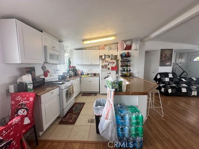 kitchen with white appliances, white cabinets, dark countertops, a kitchen bar, and light tile patterned flooring