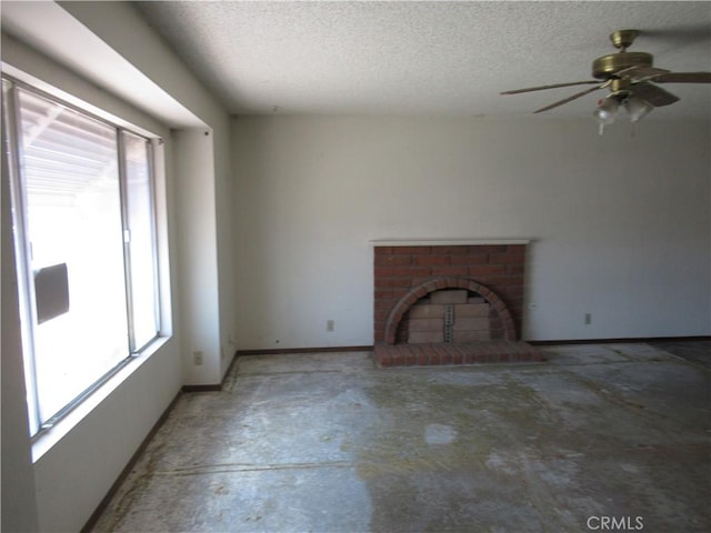 unfurnished living room with concrete floors, ceiling fan, a textured ceiling, a brick fireplace, and baseboards