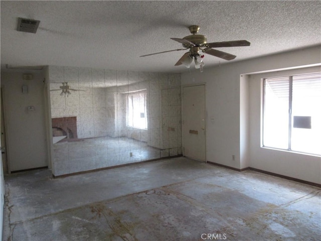 unfurnished living room with concrete flooring, ceiling fan, a textured ceiling, and healthy amount of natural light