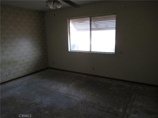 unfurnished room featuring wallpapered walls, concrete floors, a ceiling fan, and baseboards