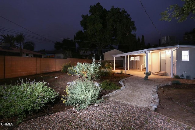 yard at night featuring fence, entry steps, and a patio area