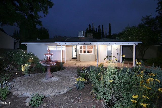back of house at night with a patio area and stucco siding