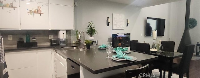 kitchen with a sink, tasteful backsplash, white cabinetry, dishwashing machine, and dark countertops