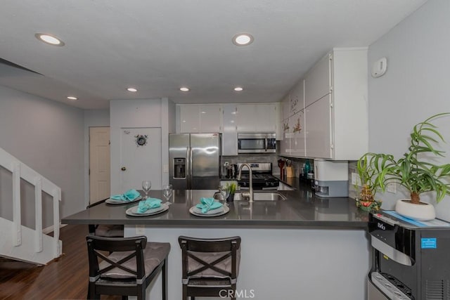 kitchen with appliances with stainless steel finishes, dark countertops, a sink, a peninsula, and recessed lighting