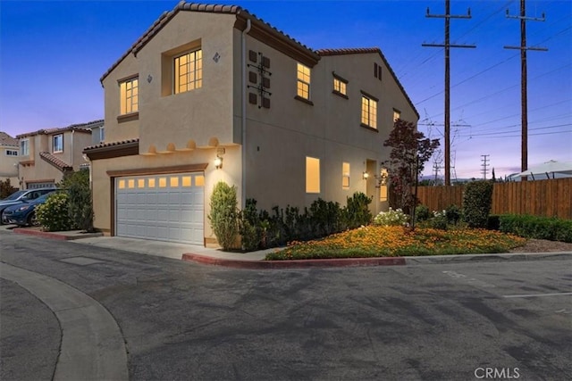 view of front of home with an attached garage, fence, stucco siding, and a tiled roof