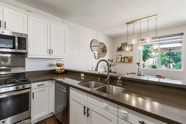 kitchen featuring stainless steel appliances, a sink, dark countertops, white cabinetry, and hanging light fixtures